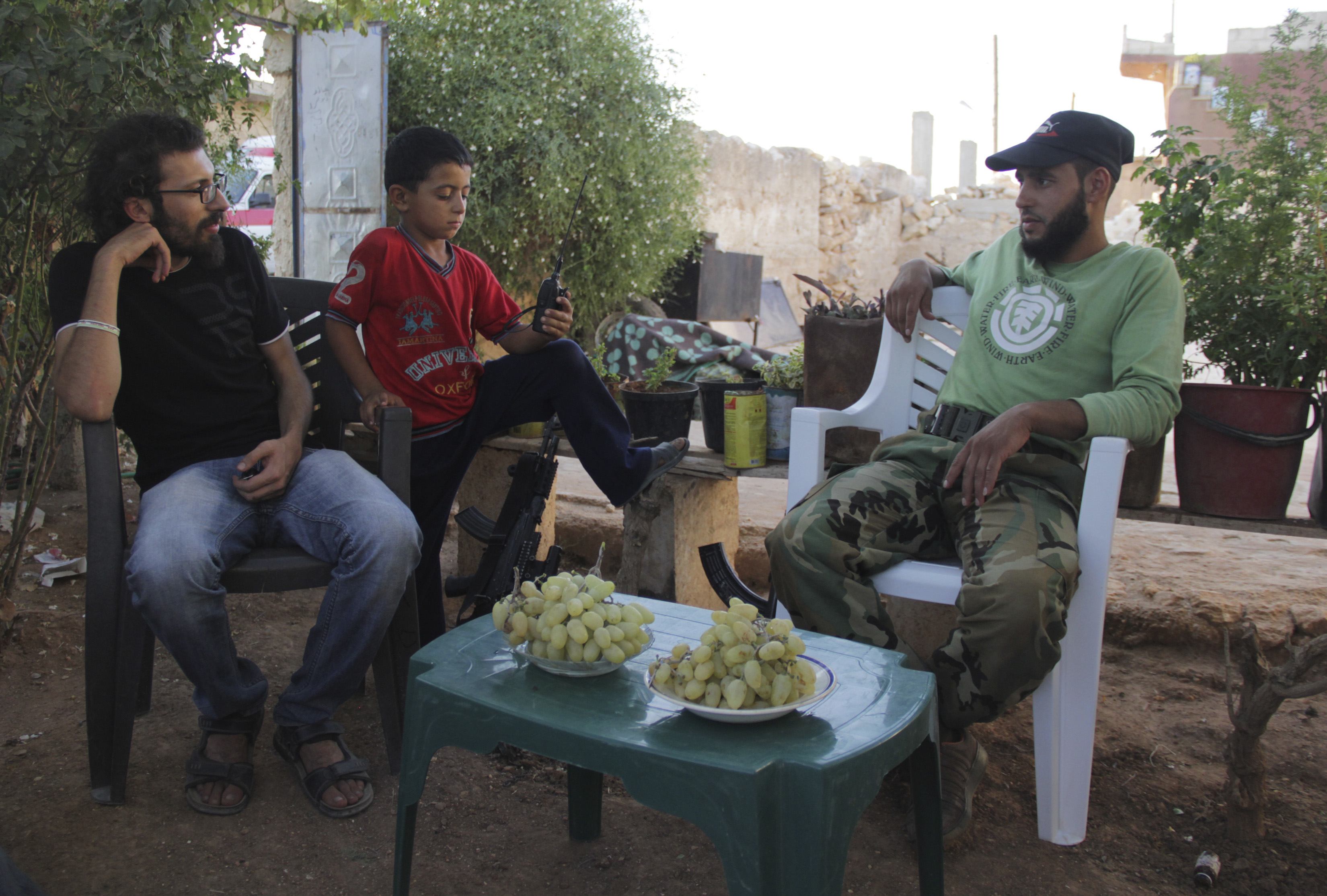 Free Syrian Army fighters sit as a boy holds a walkie talkie in Kansafra in Idlib province